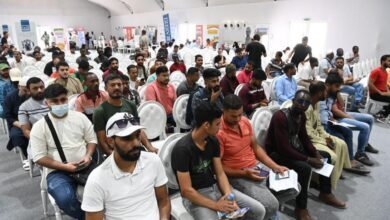 Group of people seated in a conference hall, holding documents, with banners in the background, likely related to UAE visa violation processing.