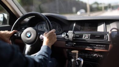 Close-up of hands on the steering wheel of a BMW while driving on a clear road.