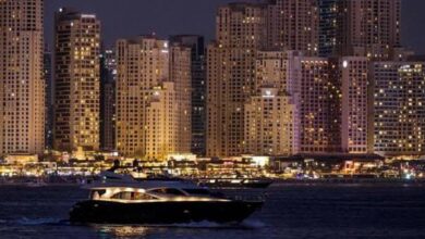 The image of a luxury yacht cruises past Dubai Marina skyscrapers illuminated at night, showcasing the city's vibrant waterfront lifestyle.