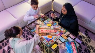 The image of a thrree people, including a child and two women, play the newly launched Riyadh edition of Monopoly at a modern indoor setting.