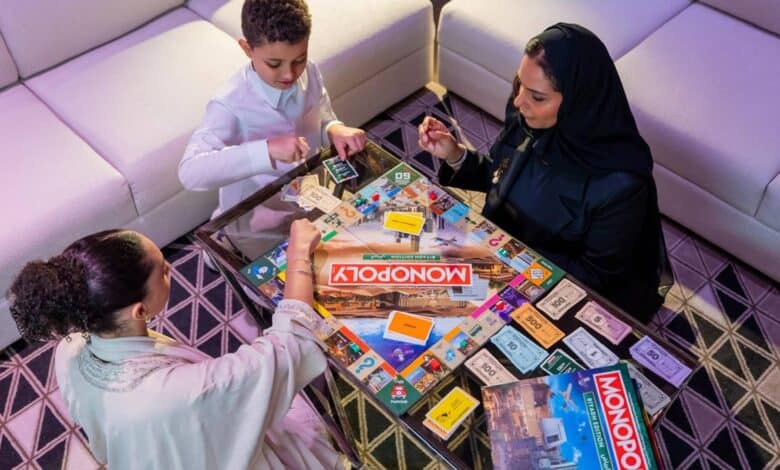 The image of a thrree people, including a child and two women, play the newly launched Riyadh edition of Monopoly at a modern indoor setting.