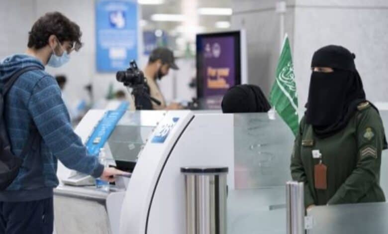 A Saudi female immigration officer in uniform processes a male passenger at an airport immigration counter.