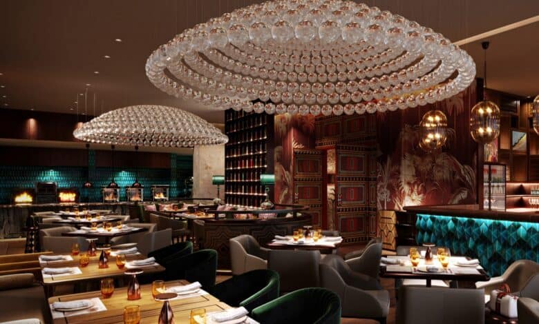 Luxurious interior of a Saudi café featuring elegant crystal chandeliers, plush seating, rich wood and patterned wall decor, with teal and gold accents. Tables are neatly set with amber glassware and napkins, creating a warm and upscale dining ambiance.