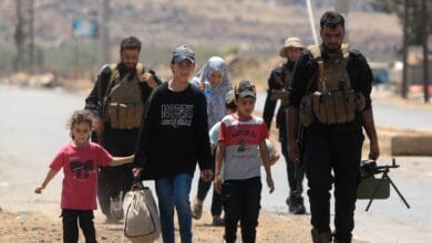 A Syrian family walks with armed escorts during displacement from Sweida.