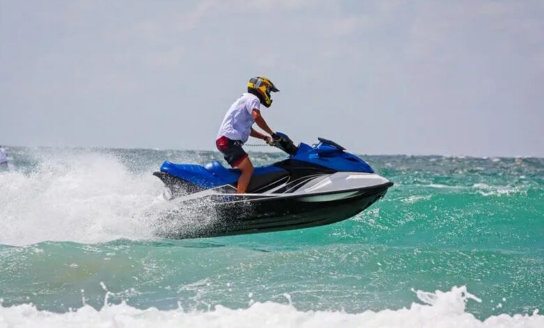 A person rides a jet ski over waves in the sea, wearing a helmet and safety gear.