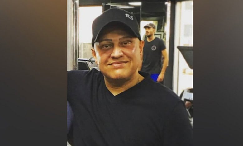 Indian businessman Abu Sabah wearing a black T-shirt and cap, smiling indoors.