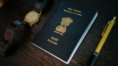 Indian passport placed on a dark wooden table with a wristwatch and a golden pen.