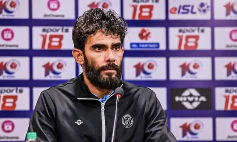 The image shows Khalid Jamil, a man with a beard and curly hair, wearing a black jacket with a logo, sitting at a press conference with microphones, surrounded by ISL and sponsor banners.