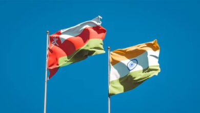 National flags of Oman and India waving against a clear blue sky, symbolising diplomatic and trade relations between the two nations.