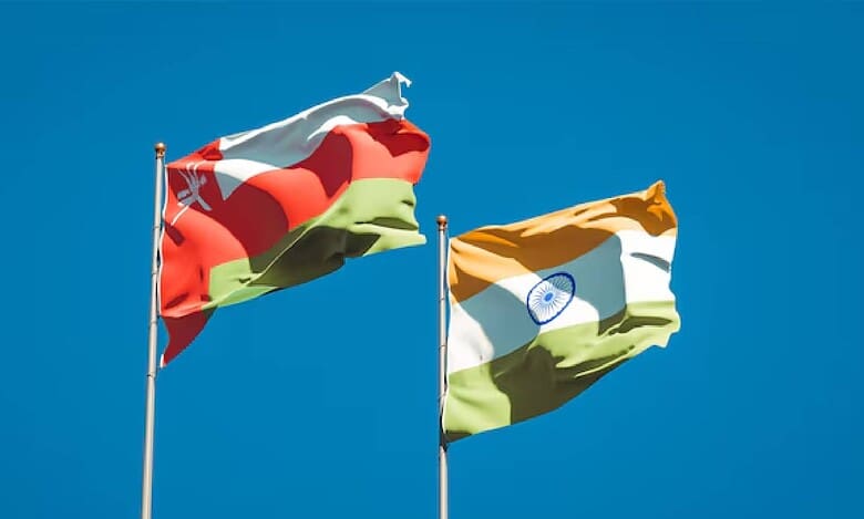 National flags of Oman and India waving against a clear blue sky, symbolising diplomatic and trade relations between the two nations.