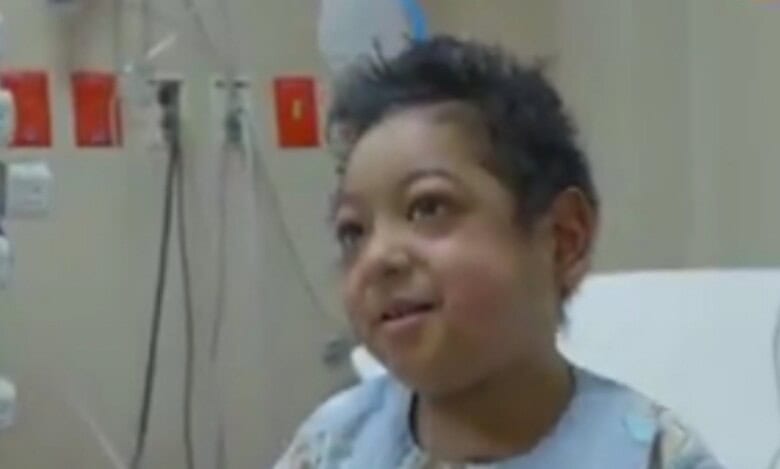Smiling 7-year-old Saudi boy in hospital gown after heart transplant.