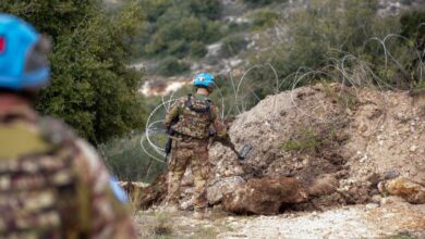 UNIFIL peacekeepers in blue helmets inspect terrain near barbed wire using a metal detector.