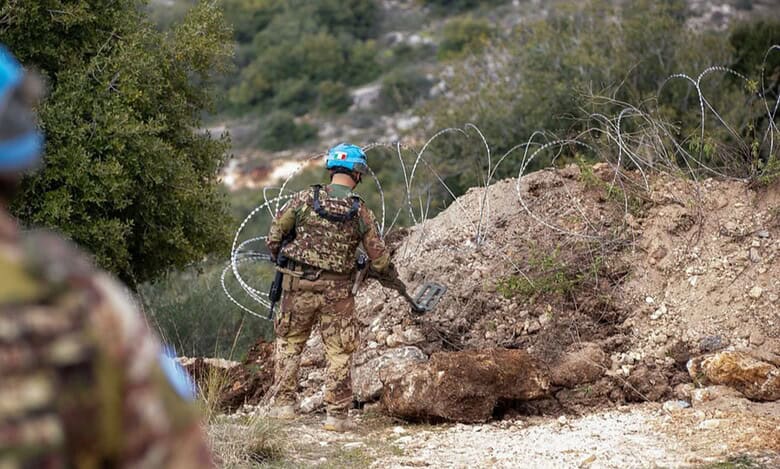 UNIFIL peacekeepers in blue helmets inspect terrain near barbed wire using a metal detector.