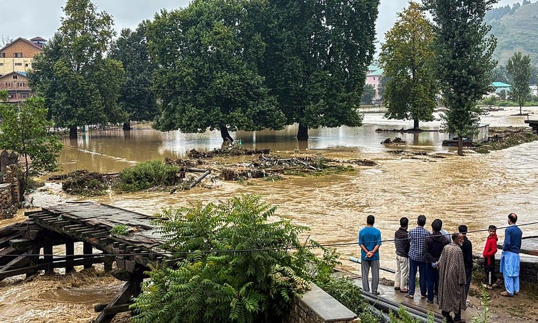 People stand near a partially damaged bridge as the Jhelum river flows in spate due to heavy rainfall in Anantnag of Jammu and Kashmir on Wednesday. (PTI Photo)