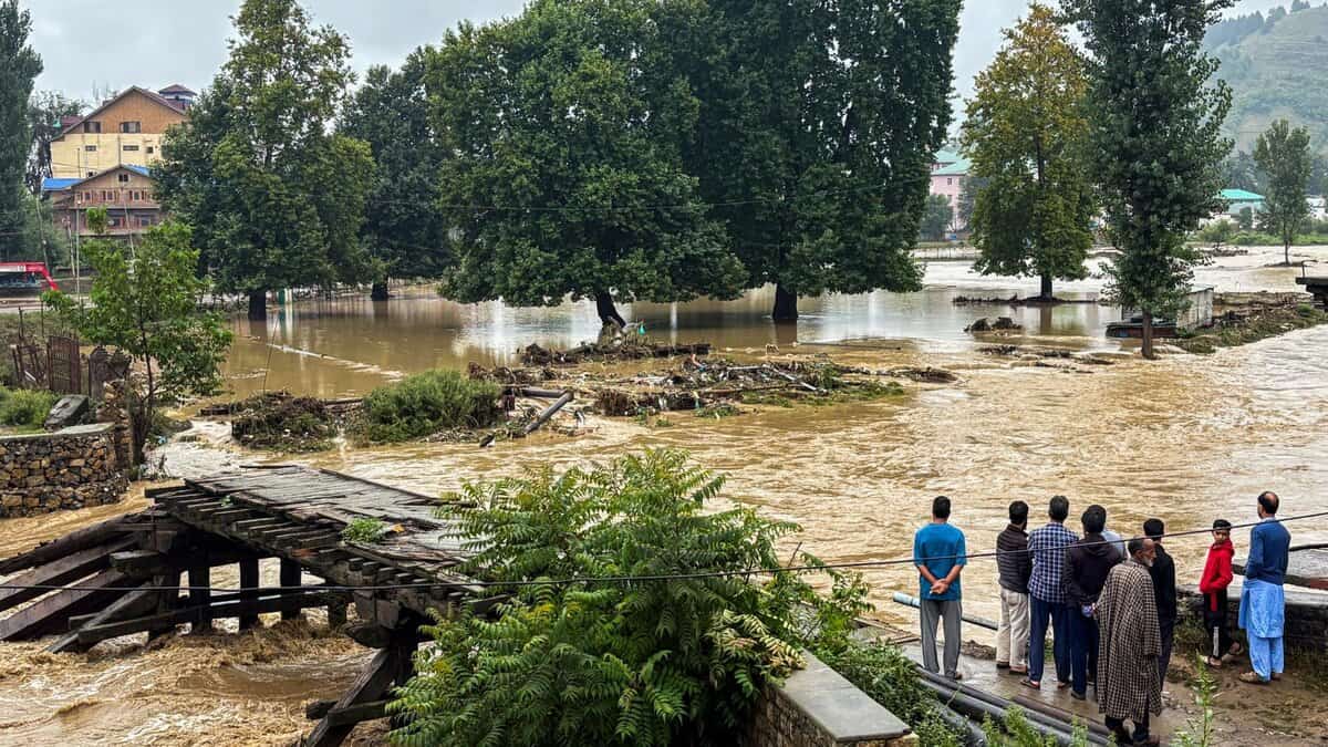 People stand near a partially damaged bridge as the Jhelum river flows in spate due to heavy rainfall in Anantnag of Jammu and Kashmir on Wednesday. (PTI Photo)