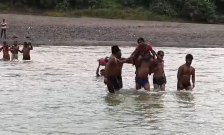 The image shows the villagers of a tribal hamlet in Kumram Bheem Asifabad district carrying an Anganwadi on shoulders across the stream as there was no medical help available on Wednesday, August 20, 2025.