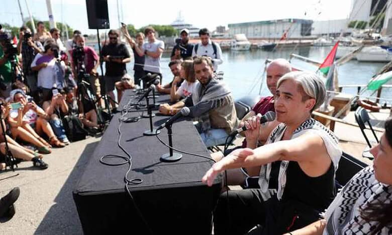 Former Barcelona mayor Ada Colau speaks at a press conference during the launch of a civilian flotilla in Barcelona, with media and supporters gathered around.