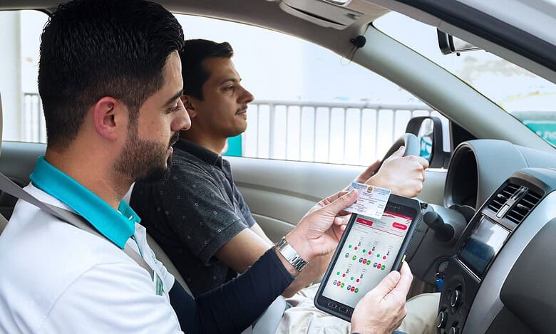Driving instructor using tablet to assess trainee driver in Dubai.