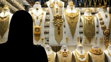 A woman in an abaya looks at an elaborate gold jewellery display in a Dubai shop, featuring ornate necklaces and accessories.