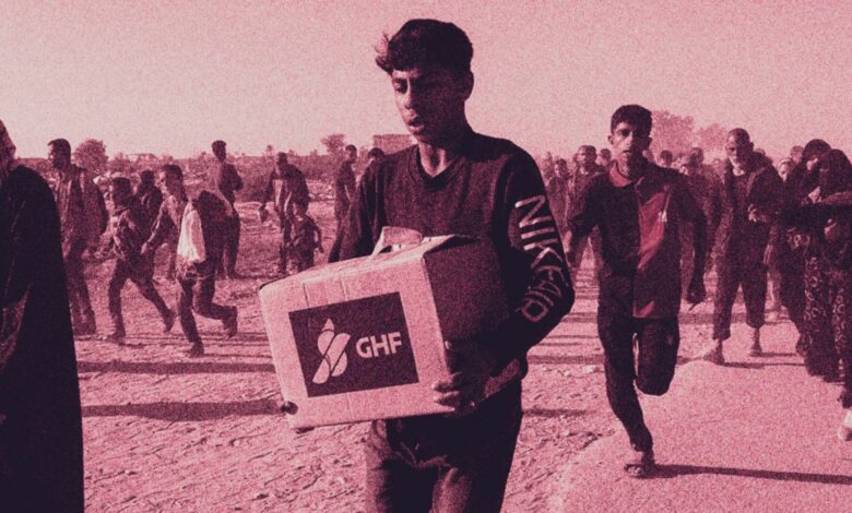 A young Palestinian man carries a Gaza Humanitarian Foundation (GHF) aid box while others walk and run behind him in a crowded, dusty area.