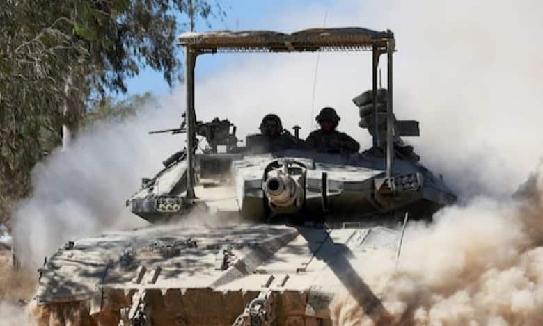 A military tank moving through a dusty environment with two soldiers visible in the turret.