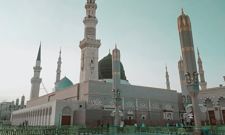 A view of the Prophet’s Mosque in Madinah, Saudi Arabia, with its iconic green dome and minarets under a clear sky.