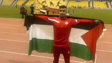 Palestinian runner Allam Abdullah Al-Amour holding the Palestinian flag on a track field.