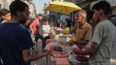 A Palestinian vendor sells food items at a street market in Gaza City, as customers examine prices amid ongoing shortages.