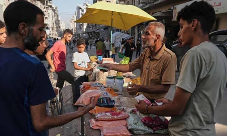 A Palestinian vendor sells food items at a street market in Gaza City, as customers examine prices amid ongoing shortages.