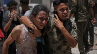 Two distressed Palestinians, one supporting the other, react emotionally while carrying a body at Shifa Hospital in Gaza City after an aid truck incident.