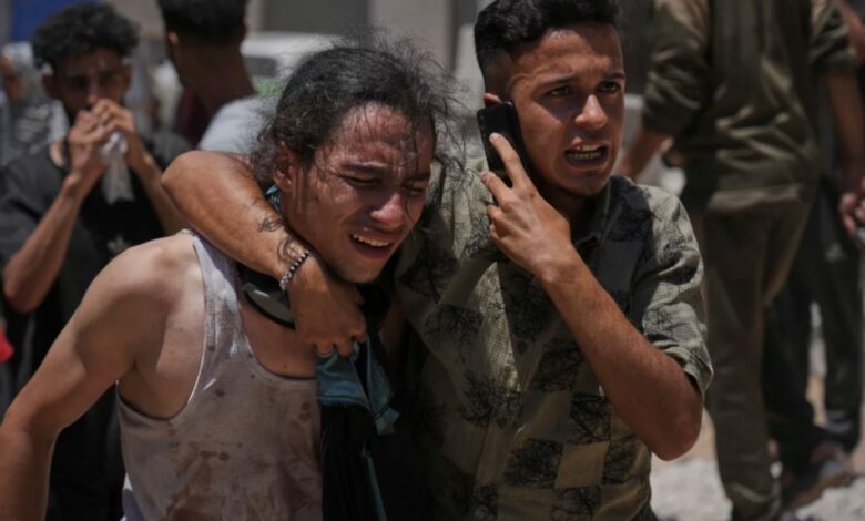 Two distressed Palestinians, one supporting the other, react emotionally while carrying a body at Shifa Hospital in Gaza City after an aid truck incident.