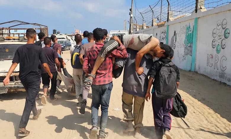 Palestinians carry wounded man near Gaza aid distribution point amid conflict.
