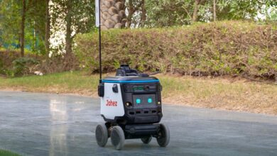 A four-wheeled autonomous food delivery robot with "Jahez" branding operating on a pathway at ROSHN Business Front.