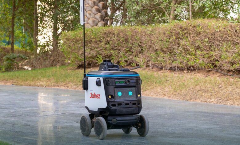 A four-wheeled autonomous food delivery robot with "Jahez" branding operating on a pathway at ROSHN Business Front.