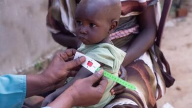 A young child receiving a health check-up, being measured for vaccination or nutritional assessment in a rural setting.