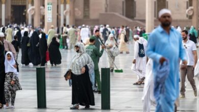 Bustling courtyard of Prophet's Mosque in Madinah with Umrah pilgrims and a cleaner amid iconic architecture.