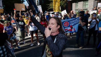 A demonstrator yells into a megaphone with others in the street outside of the National Labor Relations Board (NLRB) headquarters,