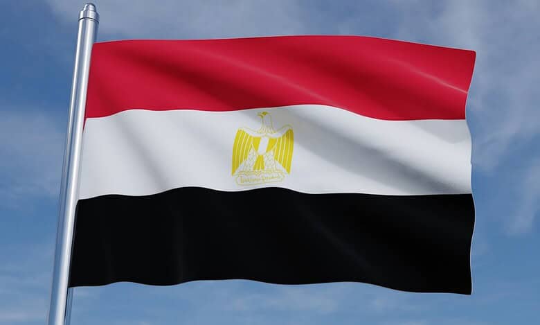 Flag of Egypt waving on a flagpole, featuring horizontal red, white, and black stripes with the golden Eagle of Saladin in the center.