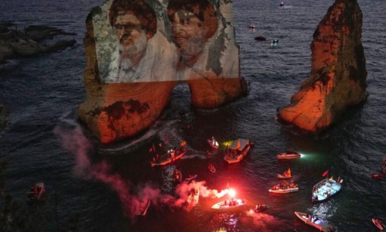 Image shows portraits of former Hezbollah leaders Hassan Nasrallah and Hashem Safieddine projected onto the Raouche sea rock during a commemorative event in Beirut, Lebanon, with boats and flares in the water, dated September 25, 2025.