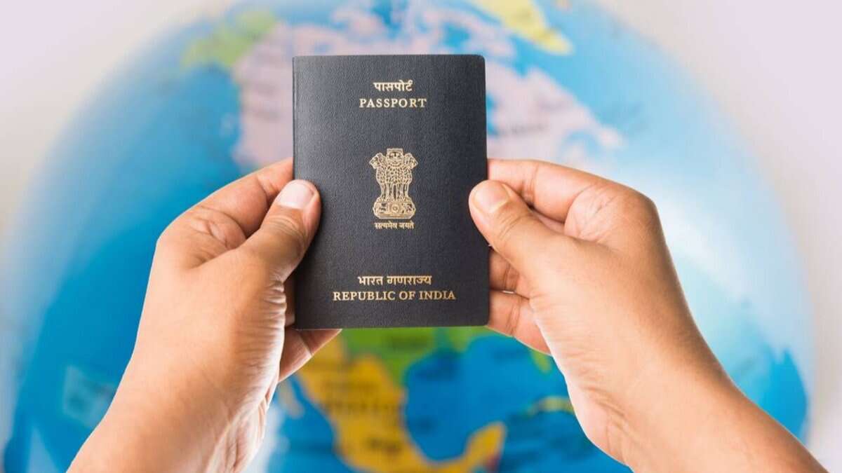 Hands holding an open Indian passport with the emblem, set against a blurred globe background.