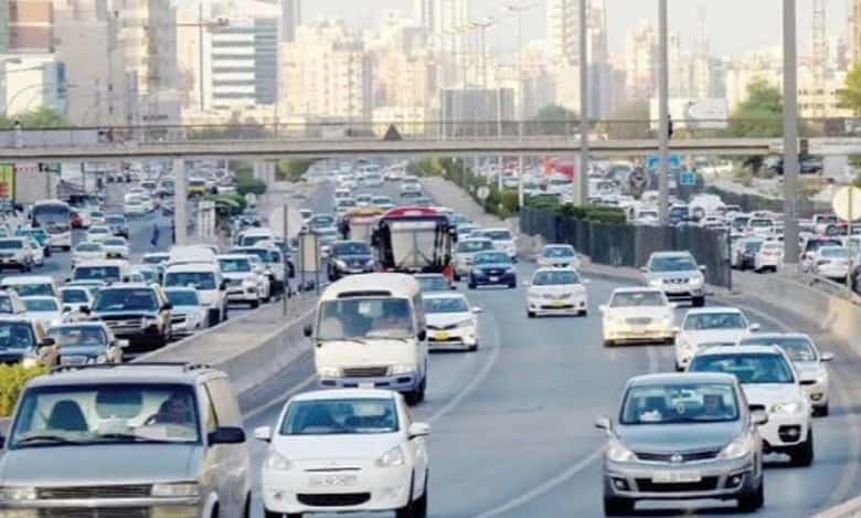 Busy multi-lane highway in Kuwait with many cars and SUVs during daylight, with city buildings in the background.
