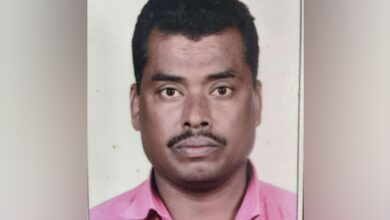 A passport-style photograph of Mohammad Rafi, a 50-year-old Indian man from Telangana with short black hair, a thin mustache, and a serious expression, wearing a pink collared shirt against a plain gray background.