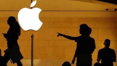Silhouettes of people outside an Apple store with a glowing Apple logo.