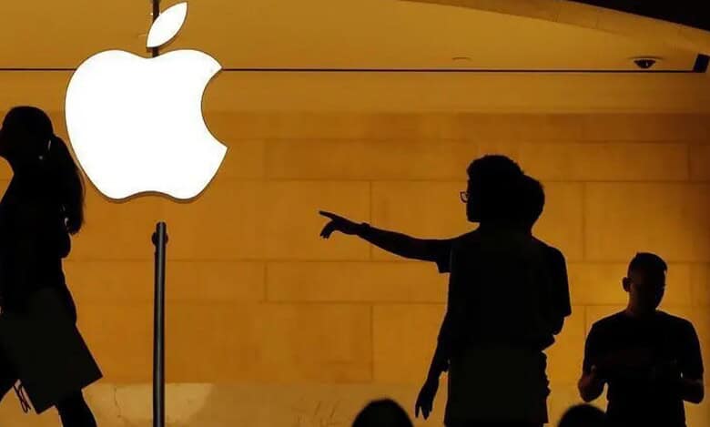 Silhouettes of people outside an Apple store with a glowing Apple logo.