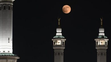 A blood moon glows above mosque minarets in Makkah, silhouetted against a dark night sky.