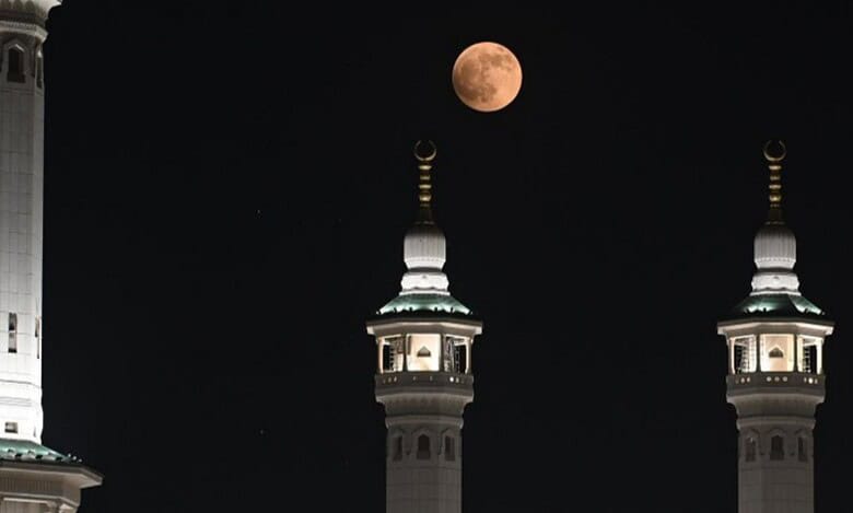 A blood moon glows above mosque minarets in Makkah, silhouetted against a dark night sky.