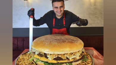 Celebrity chef CZN Burak smiles while posing with a giant burger and fries at his restaurant.