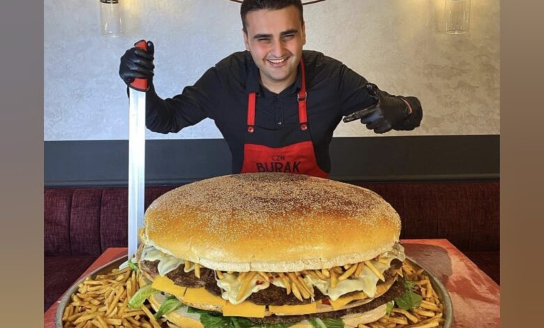 Celebrity chef CZN Burak smiles while posing with a giant burger and fries at his restaurant.
