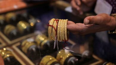 A person holding several intricately designed gold bangles in a jewellery shop, with more bangles displayed in a glass case below.