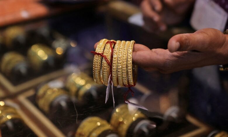 A person holding several intricately designed gold bangles in a jewellery shop, with more bangles displayed in a glass case below.